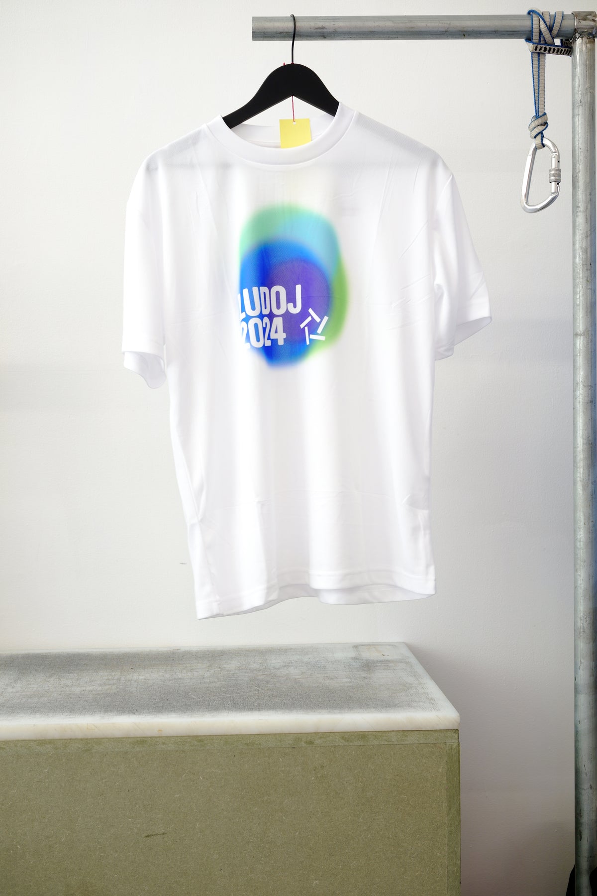 White short-sleeve T-shirt hanging on a black hanger. Featuring a colorful graphic, against white background.