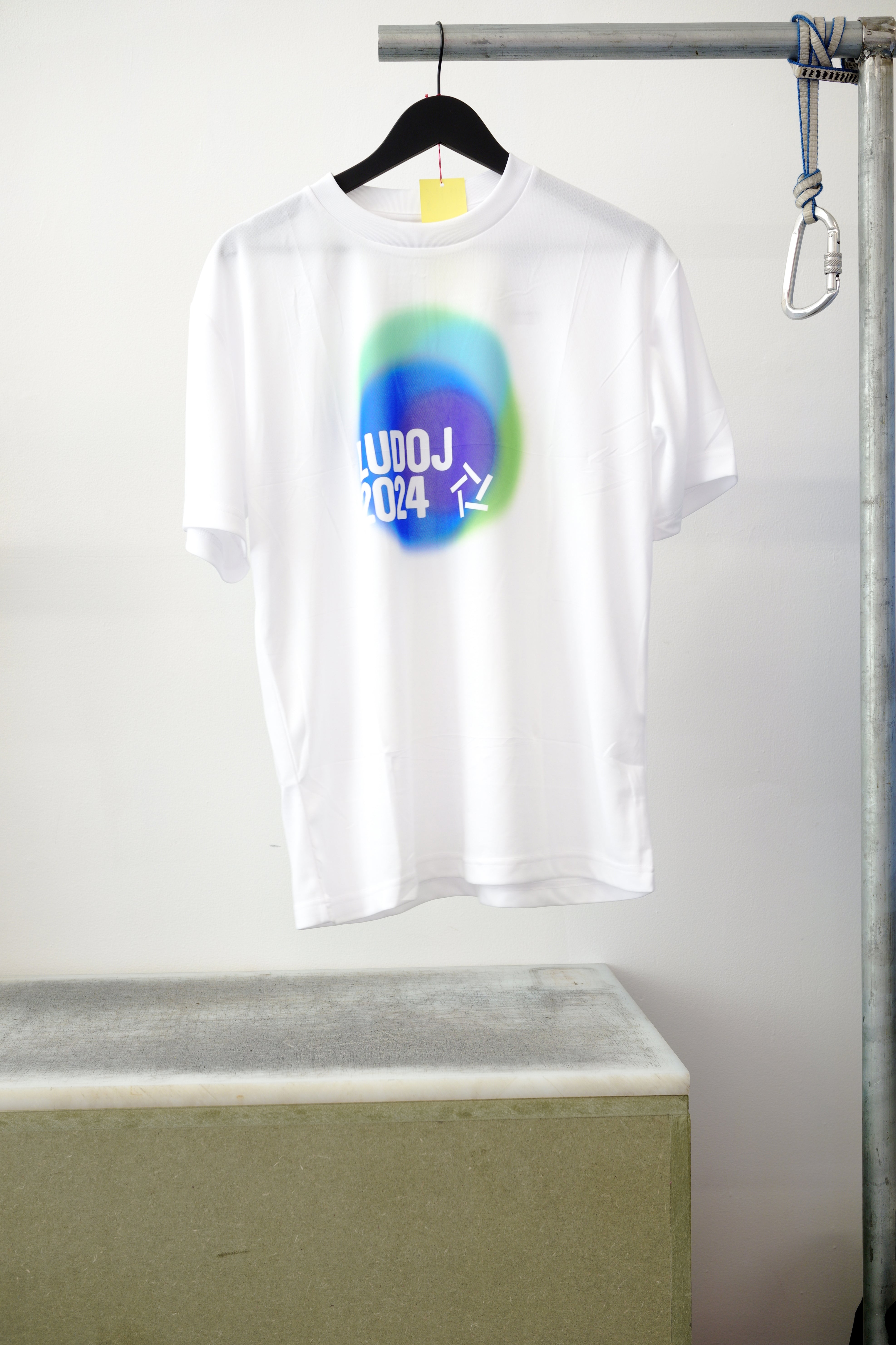 White short-sleeve T-shirt hanging on a black hanger. Featuring a colorful graphic, against white background.