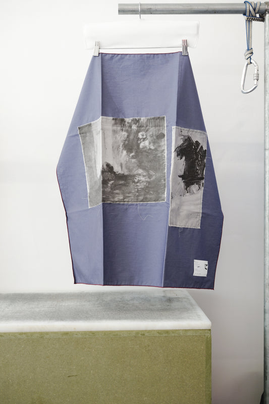 A blue foulard with burgandy grid and two print panels hanging from a metal hanger on a clothing rack, positioned above a concrete block against a white wall.