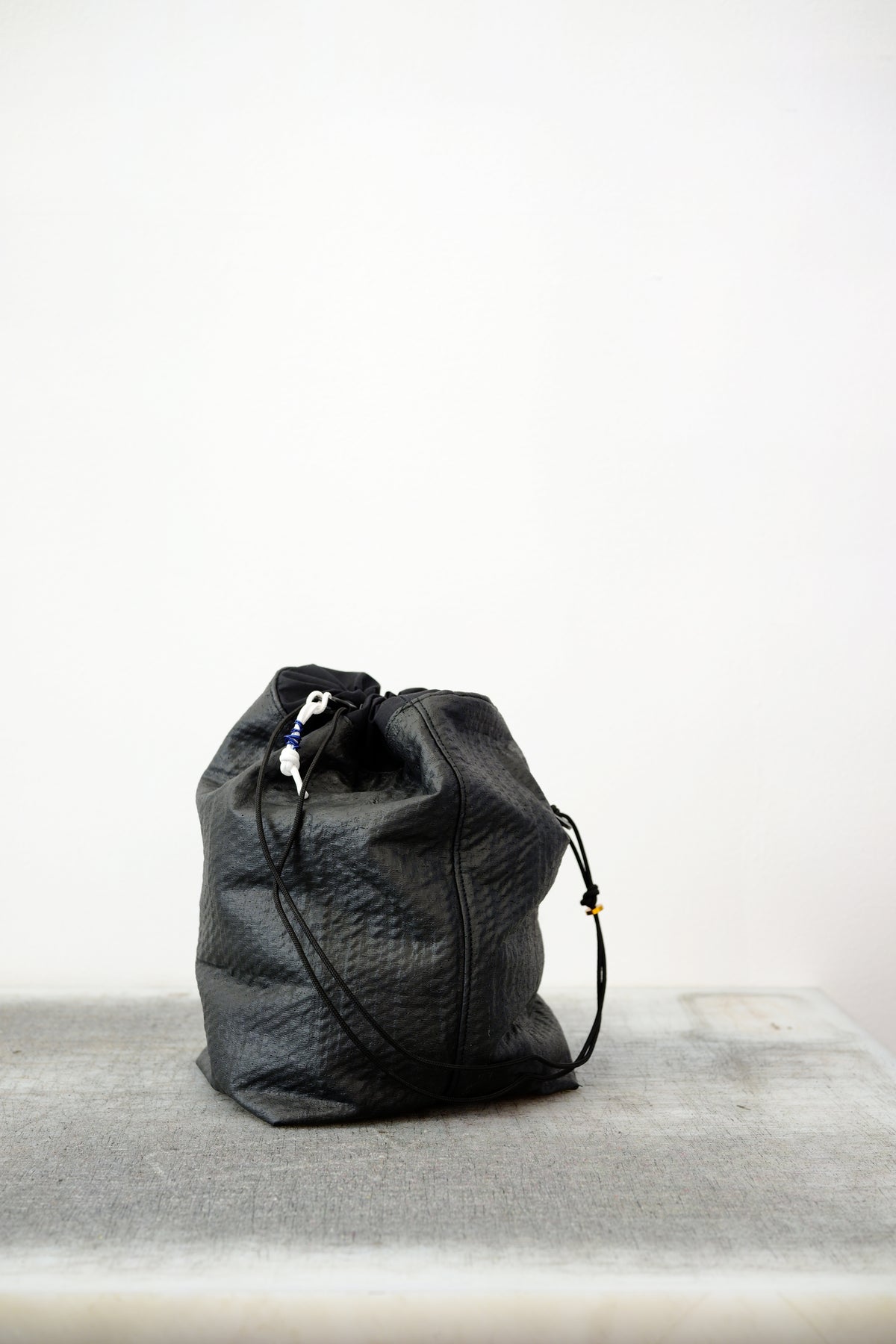 Black drawstring bag with white drawstrings and GR10K logo patch, against a plain white wall.