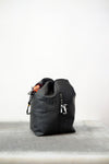 Black drawstring bag with white drawstrings and GR10K logo patch, against a plain white wall.