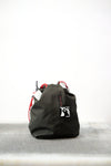 Black drawstring bag with red drawstrings and GR10K logo patch, against a plain white wall.