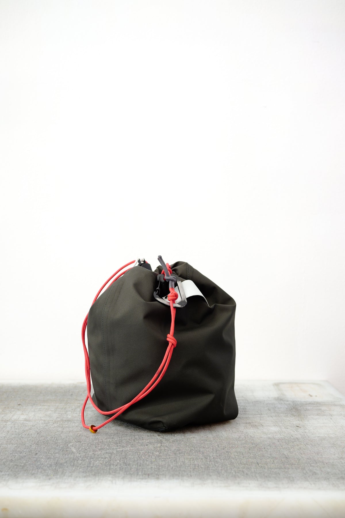 Black drawstring bag with red drawstrings and GR10K logo patch, against a plain white wall.