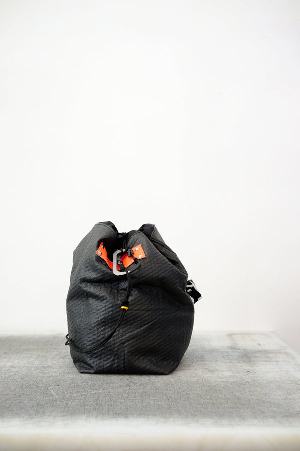 Black drawstring bag with white drawstrings and GR10K logo patch, against a plain white wall.