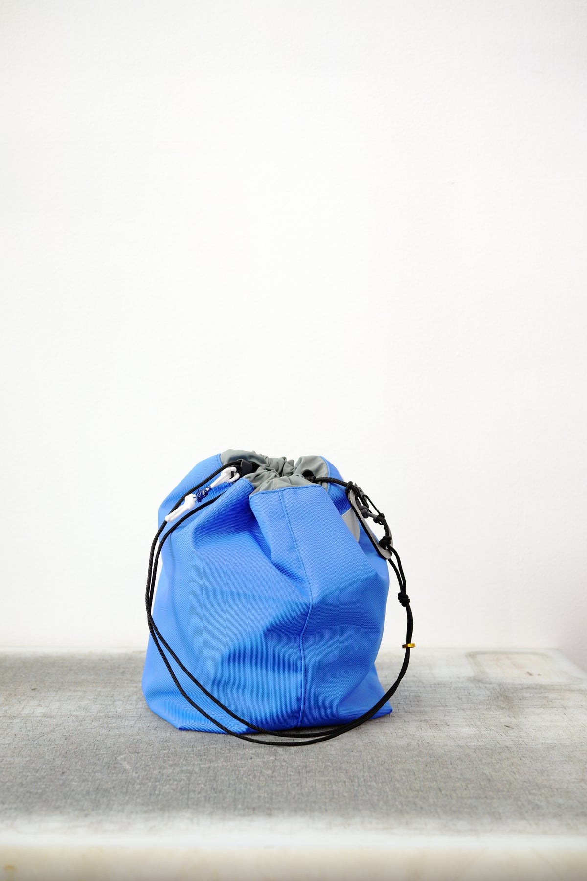 bright blue drawstring bag with white drawstrings and GR10K logo patch, against a plain white wall.