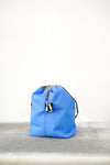 bright blue drawstring bag with white drawstrings and GR10K logo patch, against a plain white wall.