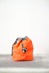 Orange drawstring bag with white drawstrings and GR10K logo patch, against a plain white wall.