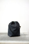 Grey drawstring bag with black drawstrings and GR10K logo patch, against a plain white wall.