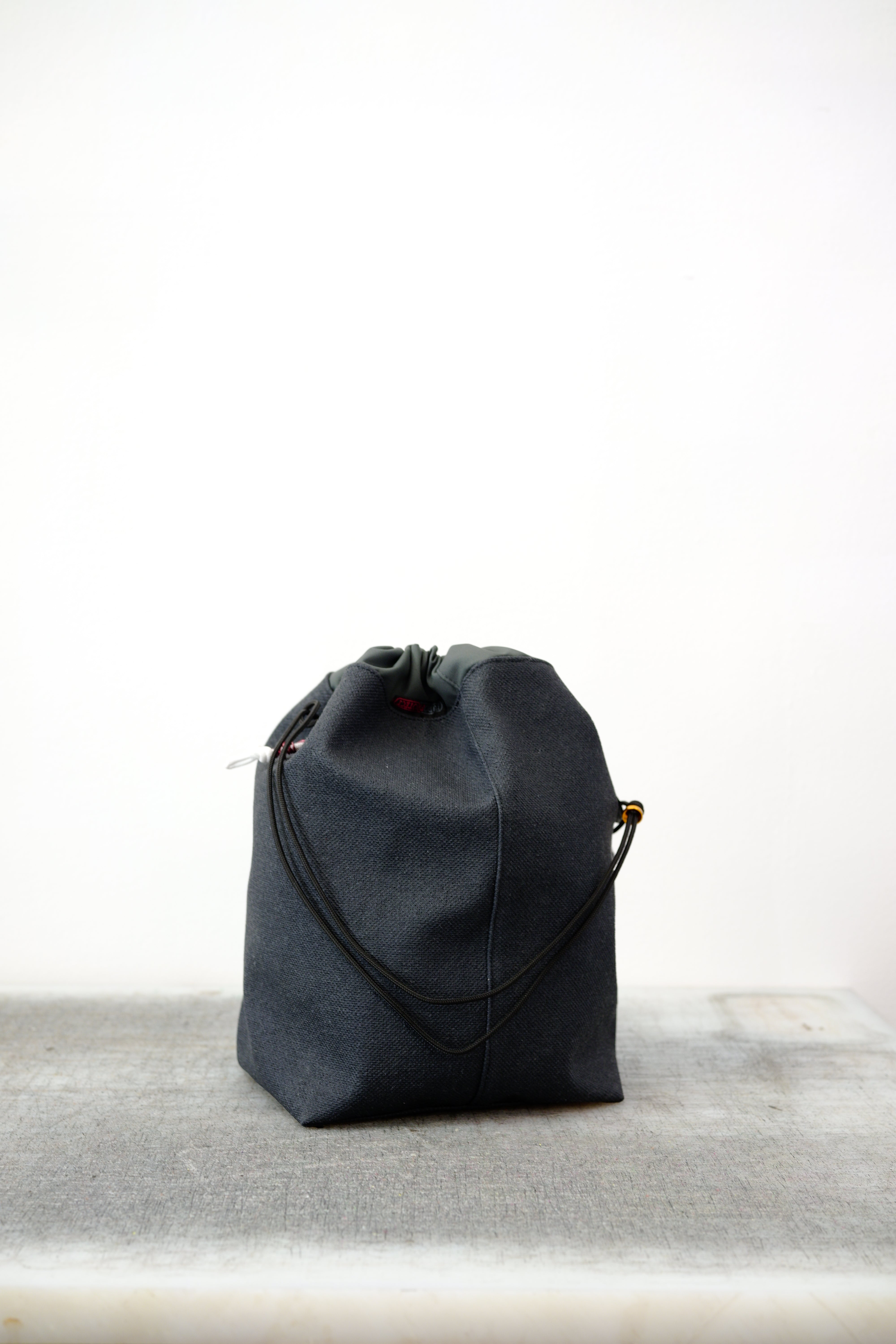 Grey drawstring bag with black drawstrings and GR10K logo patch, against a plain white wall.