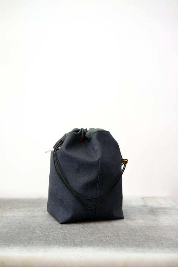 Grey drawstring bag with black drawstrings and GR10K logo patch, against a plain white wall.
