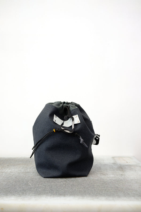 Grey drawstring bag with black drawstrings and GR10K logo patch, against a plain white wall.