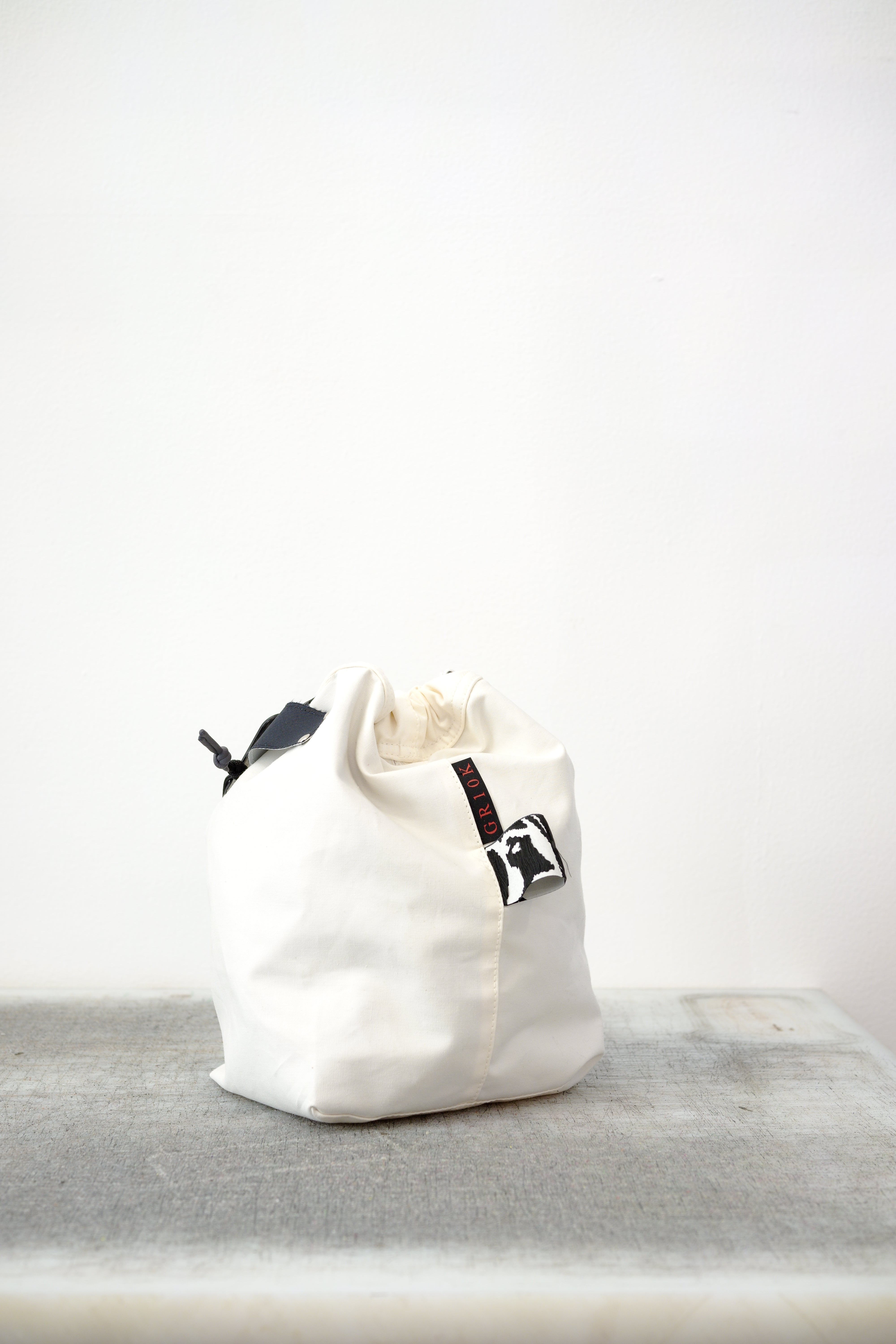 white drawstring bag with white drawstrings and GR10K logo patch, against a plain white wall.