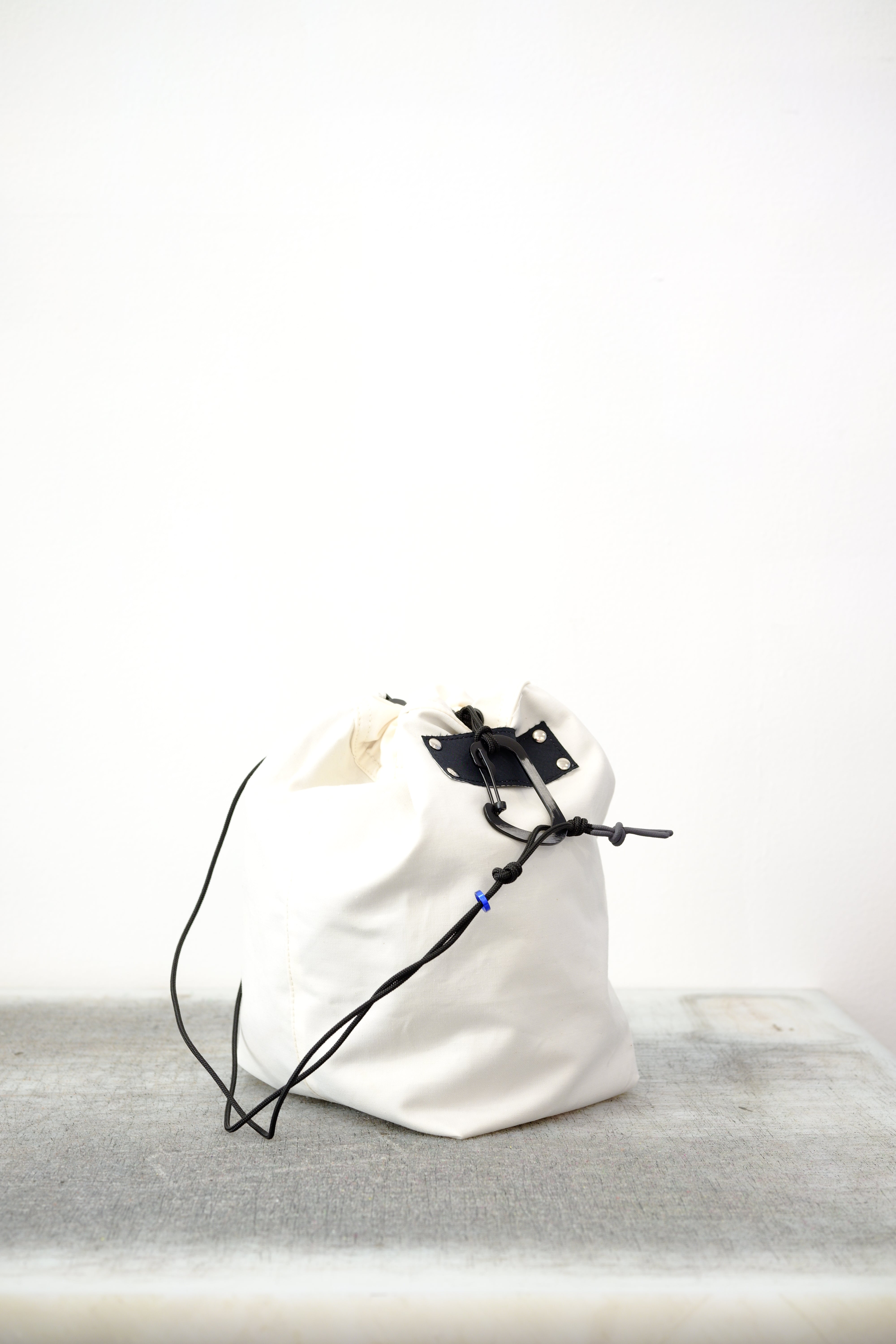 white drawstring bag with white drawstrings and GR10K logo patch, against a plain white wall.