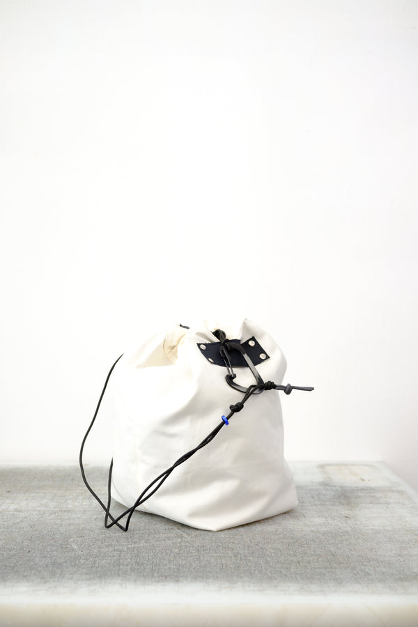 white drawstring bag with white drawstrings and GR10K logo patch, against a plain white wall.