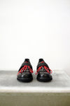 Black leather shoes with red laced detailing and silver studs, against a white background.