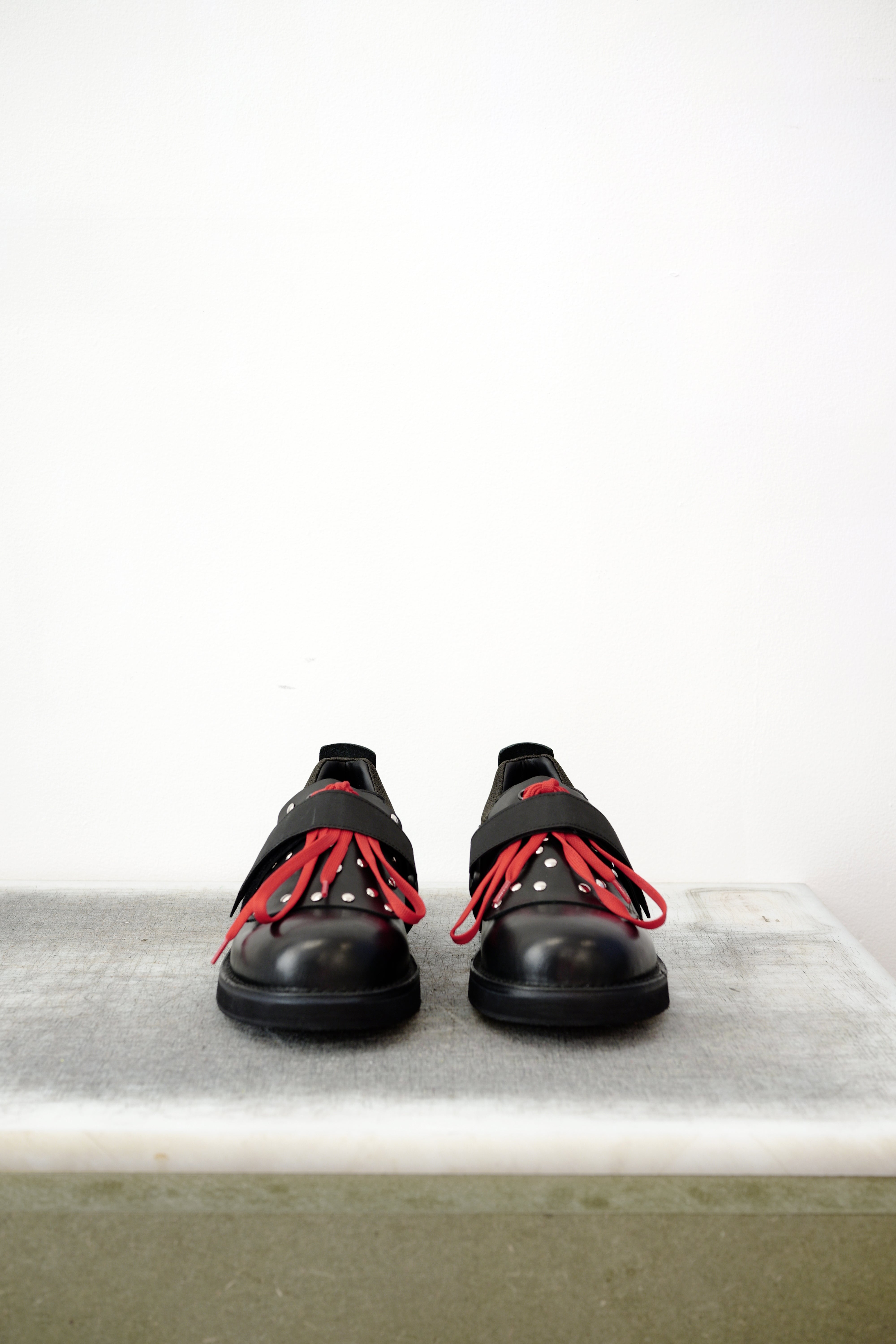 Black leather shoes with red laced detailing and silver studs, against a white background.