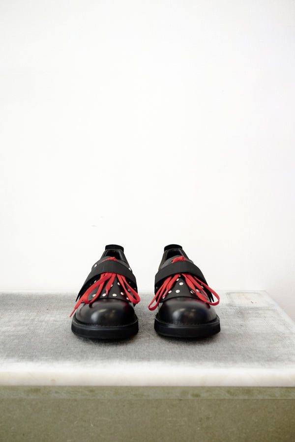 Black leather shoes with red laced detailing and silver studs, against a white background.