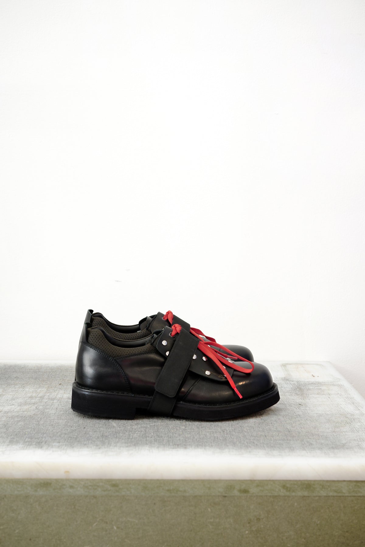 Black leather shoes with red laced detailing and silver studs, against a white background.