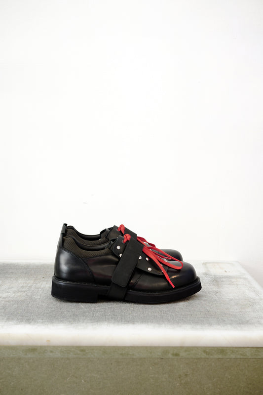 Black leather shoes with red laced detailing and silver studs, against a white background.