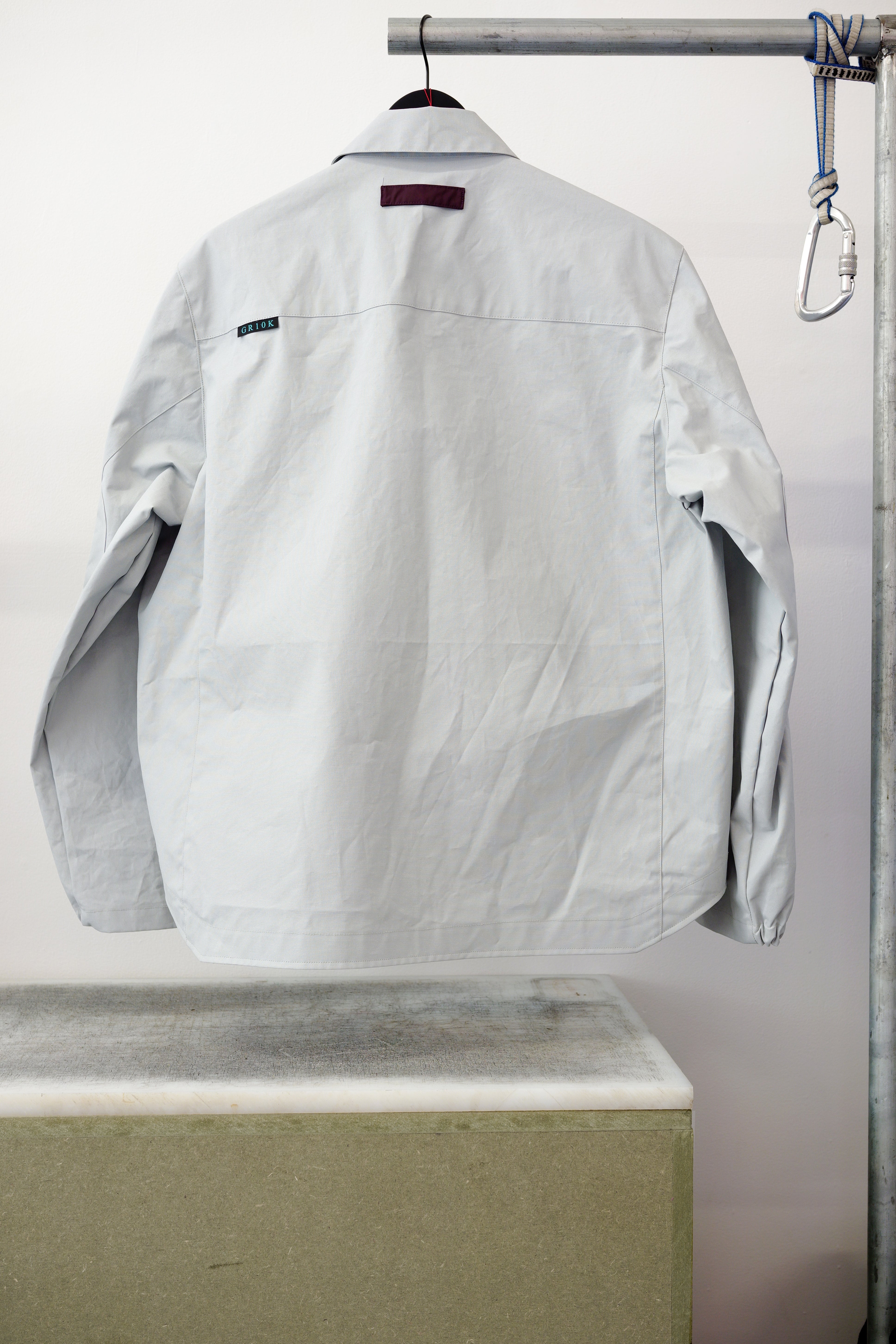 Gray utility overshirt with a pointed collar, button front, and two large chest flap pockets, hanging on a black hanger against white background