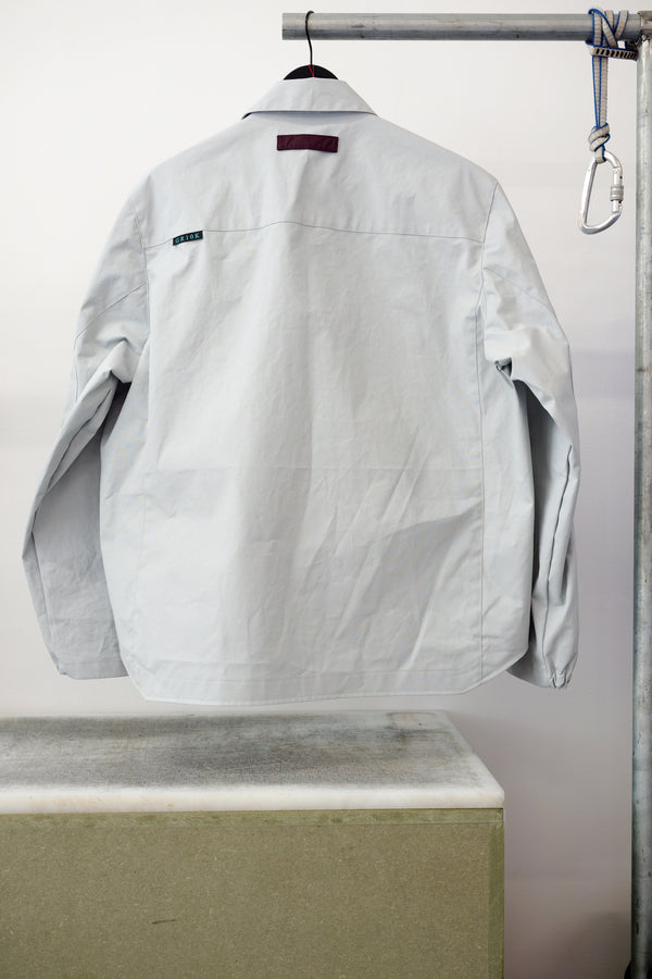 Gray utility overshirt with a pointed collar, button front, and two large chest flap pockets, hanging on a black hanger against white background