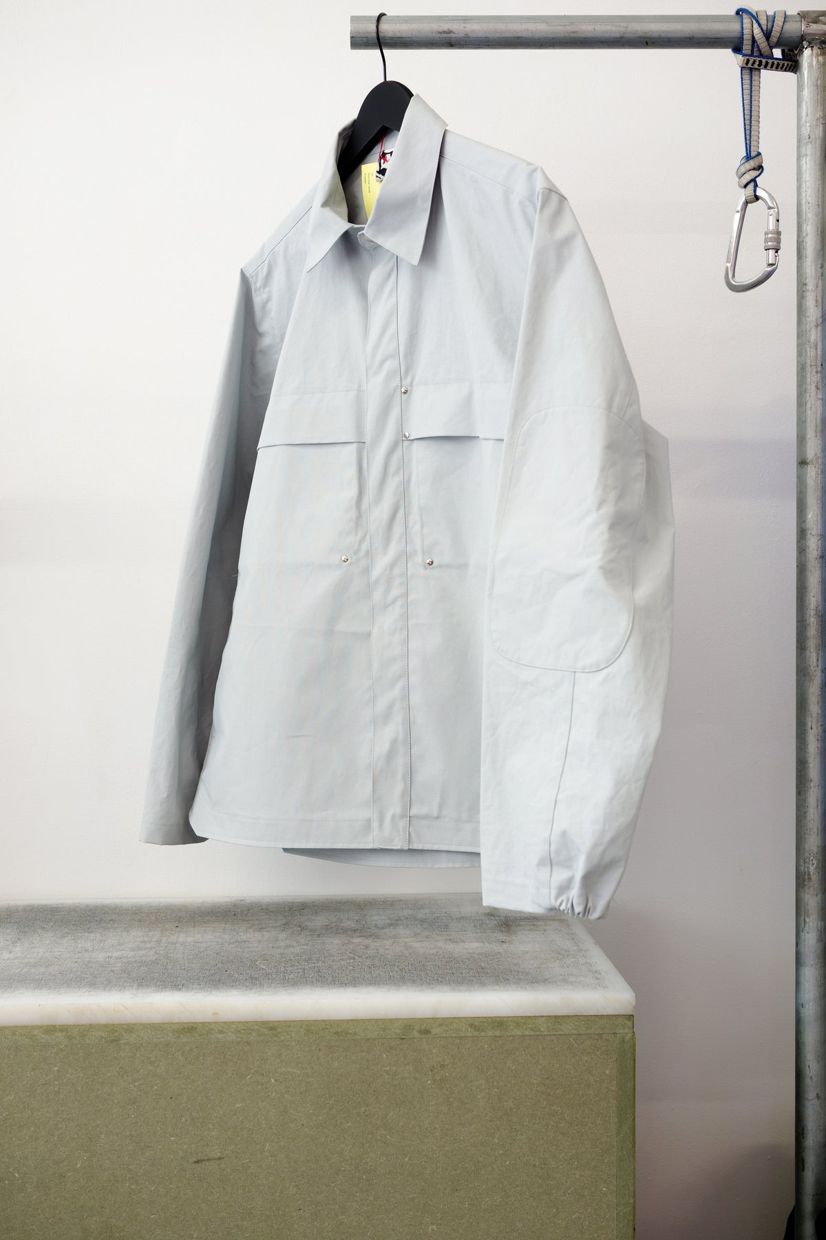 Gray utility overshirt with a pointed collar, button front, and two large chest flap pockets, hanging on a black hanger against white background