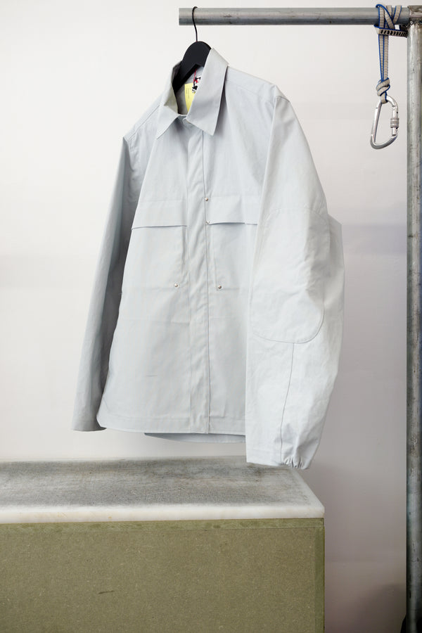 Gray utility overshirt with a pointed collar, button front, and two large chest flap pockets, hanging on a black hanger against white background