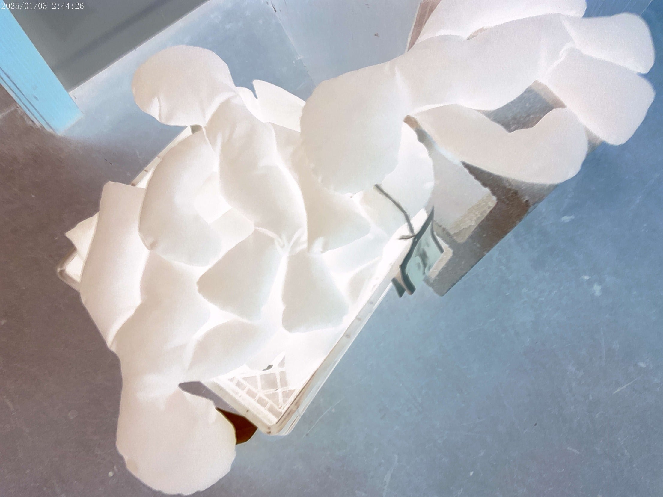 A white, cloud-like plush or padded toy with segmented, puffy sections, photographed from above on a gray surface.