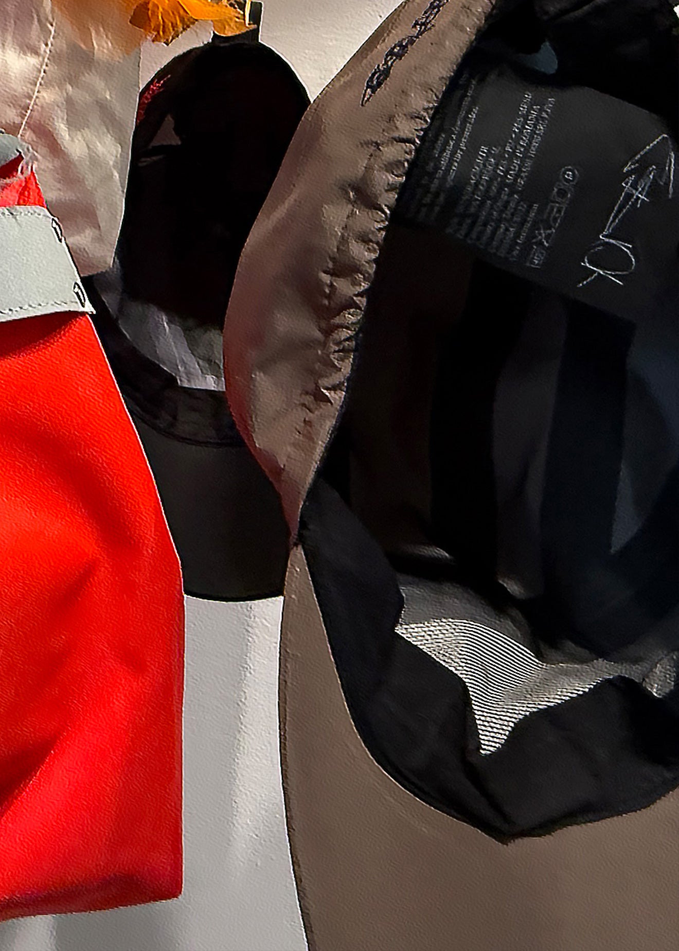 Close-up of a beige and black puffer jacket showing the interior lining and a black hangtag, with other garments partially visible in the background.