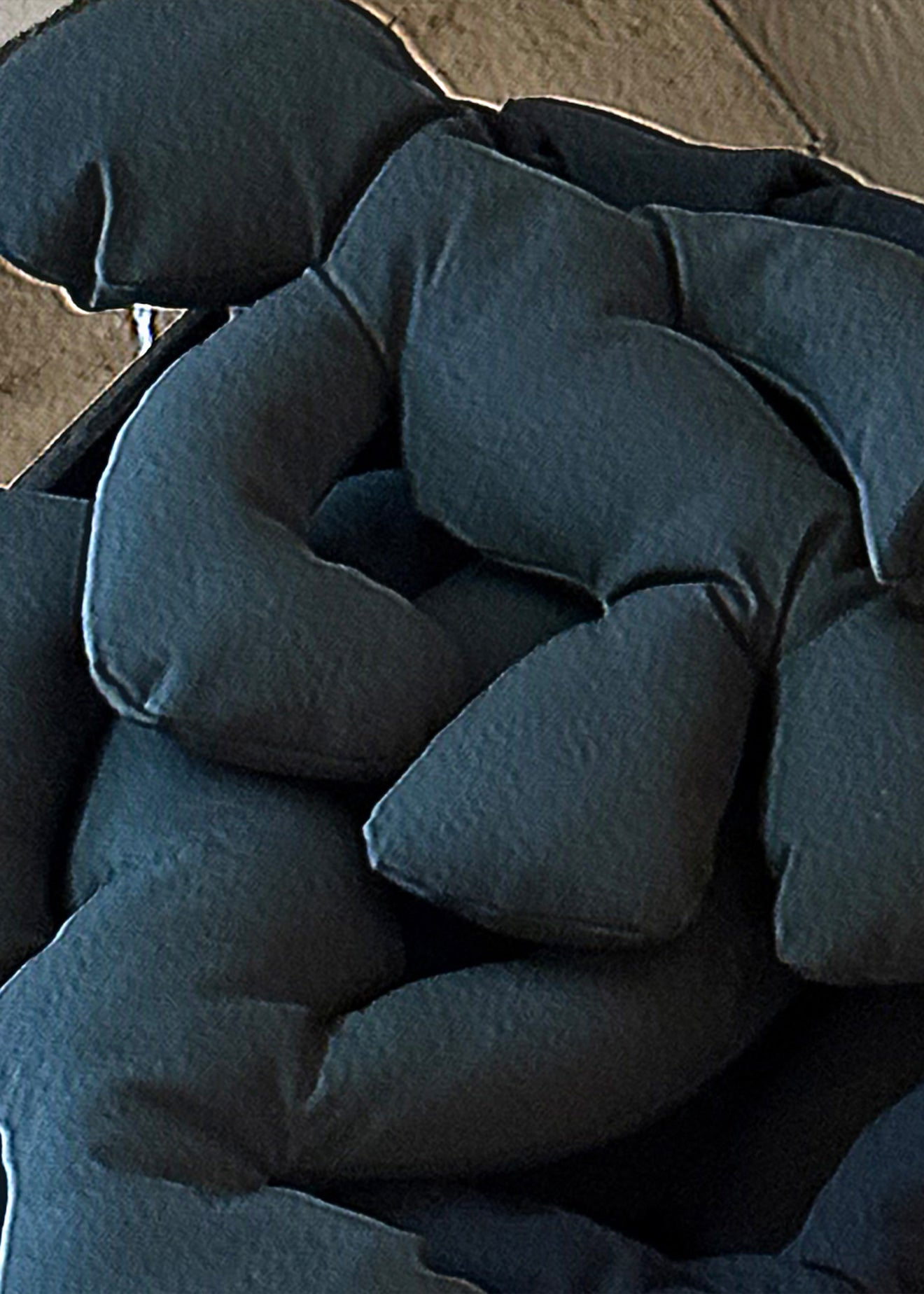 A close-up of a dark charcoal gray or black textured fabric cushion or pillow with padded, segmented sections.
