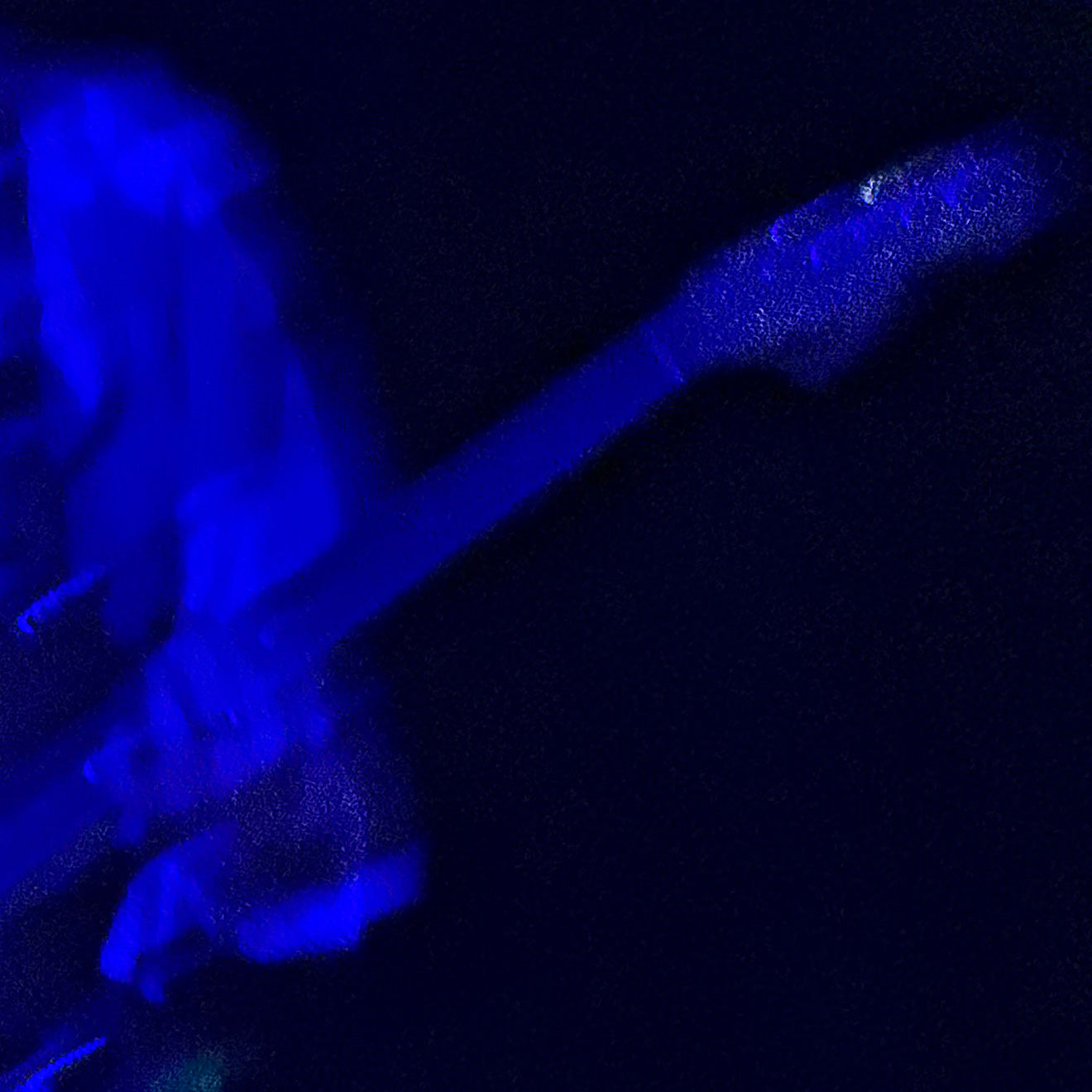 A close-up, low-light photograph of a person holding a guitar, during Kim Gordon Performance at FW:B music festival
