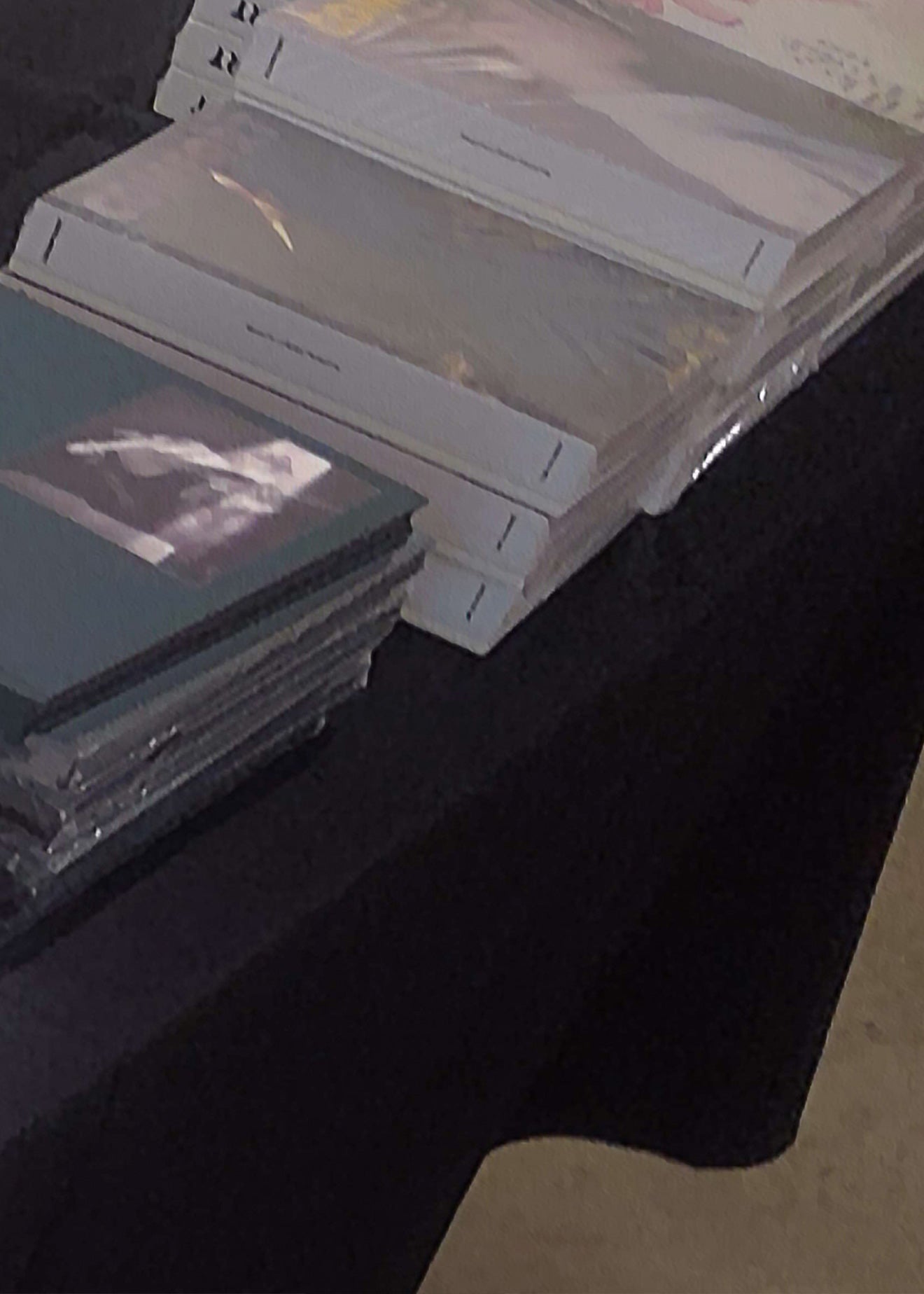 Stacks of printed books or albums wrapped in clear plastic, arranged on a black tablecloth-covered table in an indoor setting.