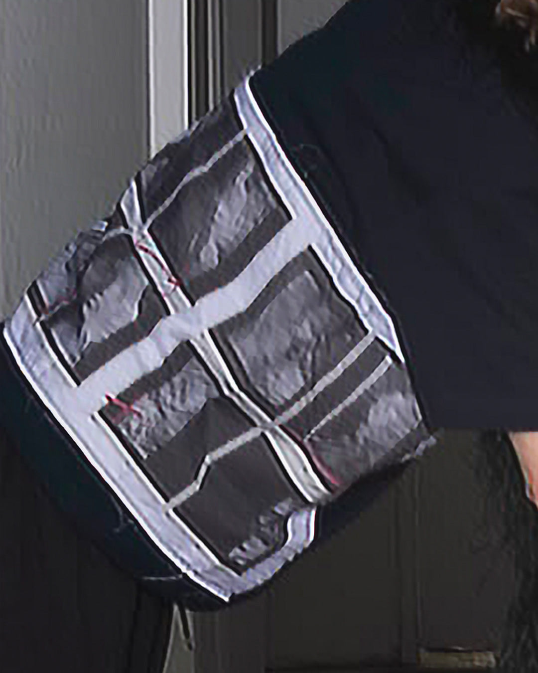 A close-up of a person wearing a dark  shirt with a large, square-patterned gray and white patchwork fabric panel attached.