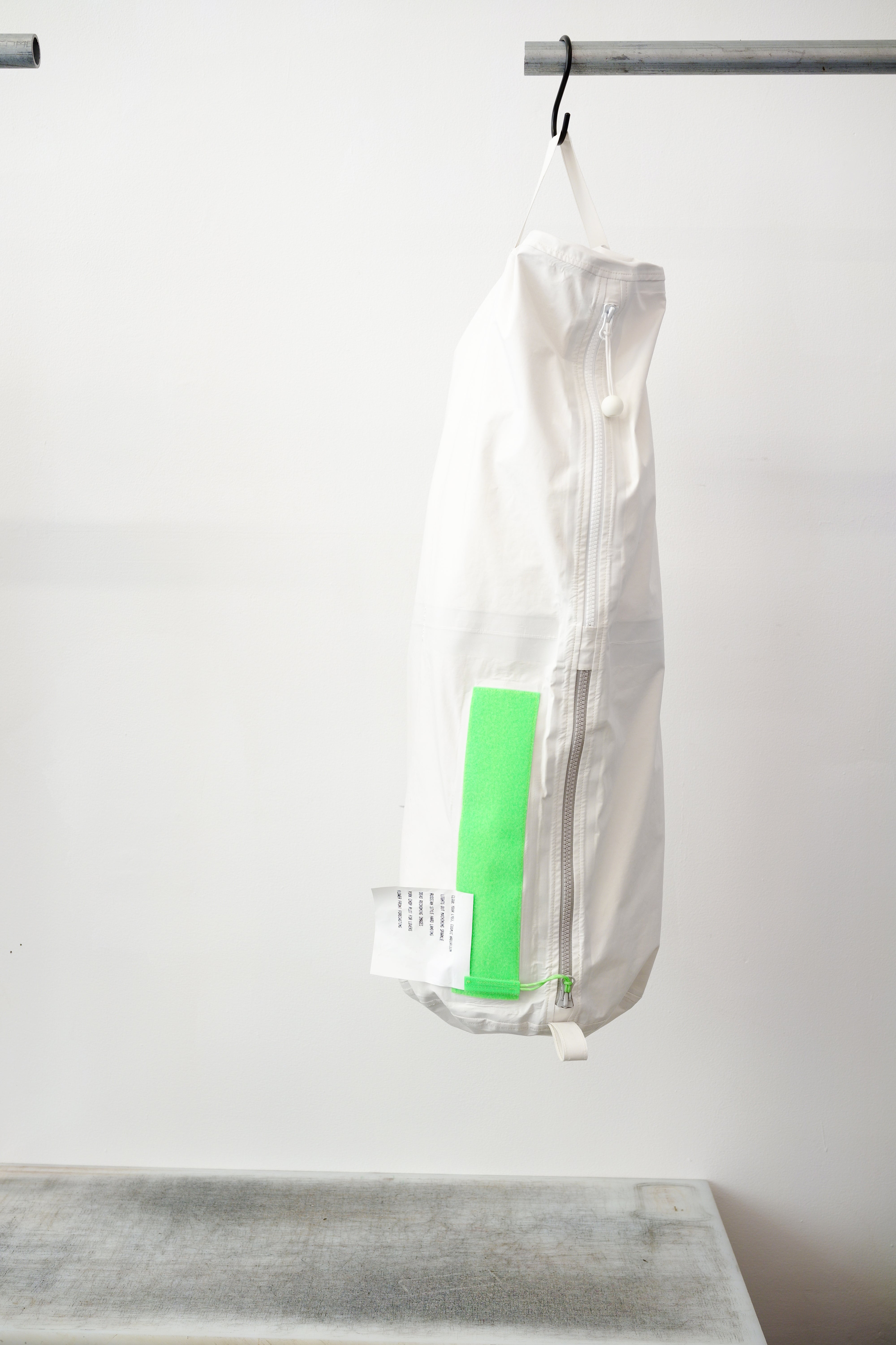 white kit bag with a lime rectangular accent panel, hanging from a black hook against a plain white wall.