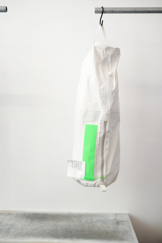 white kit bag with a lime rectangular accent panel, hanging from a black hook against a plain white wall.