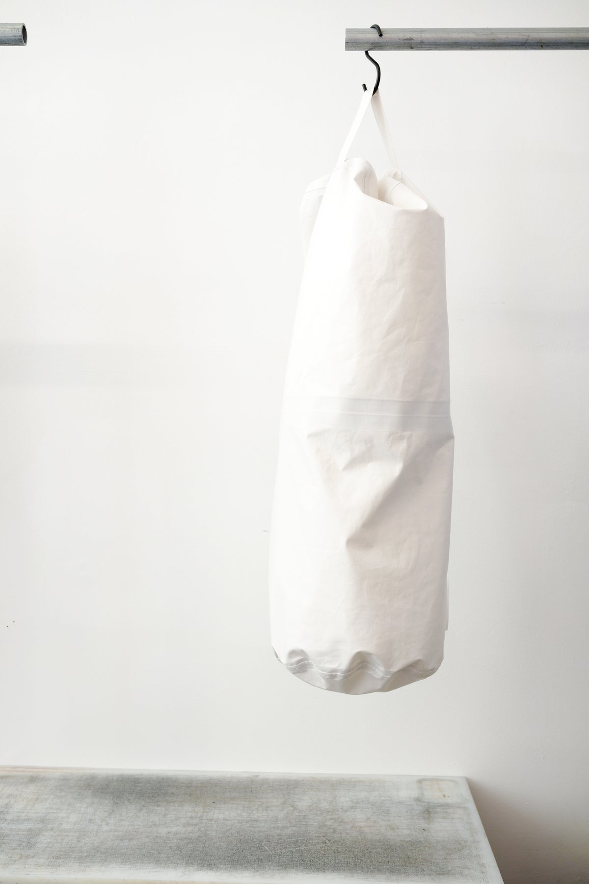 white kit bag with a lime rectangular accent panel, hanging from a black hook against a plain white wall.