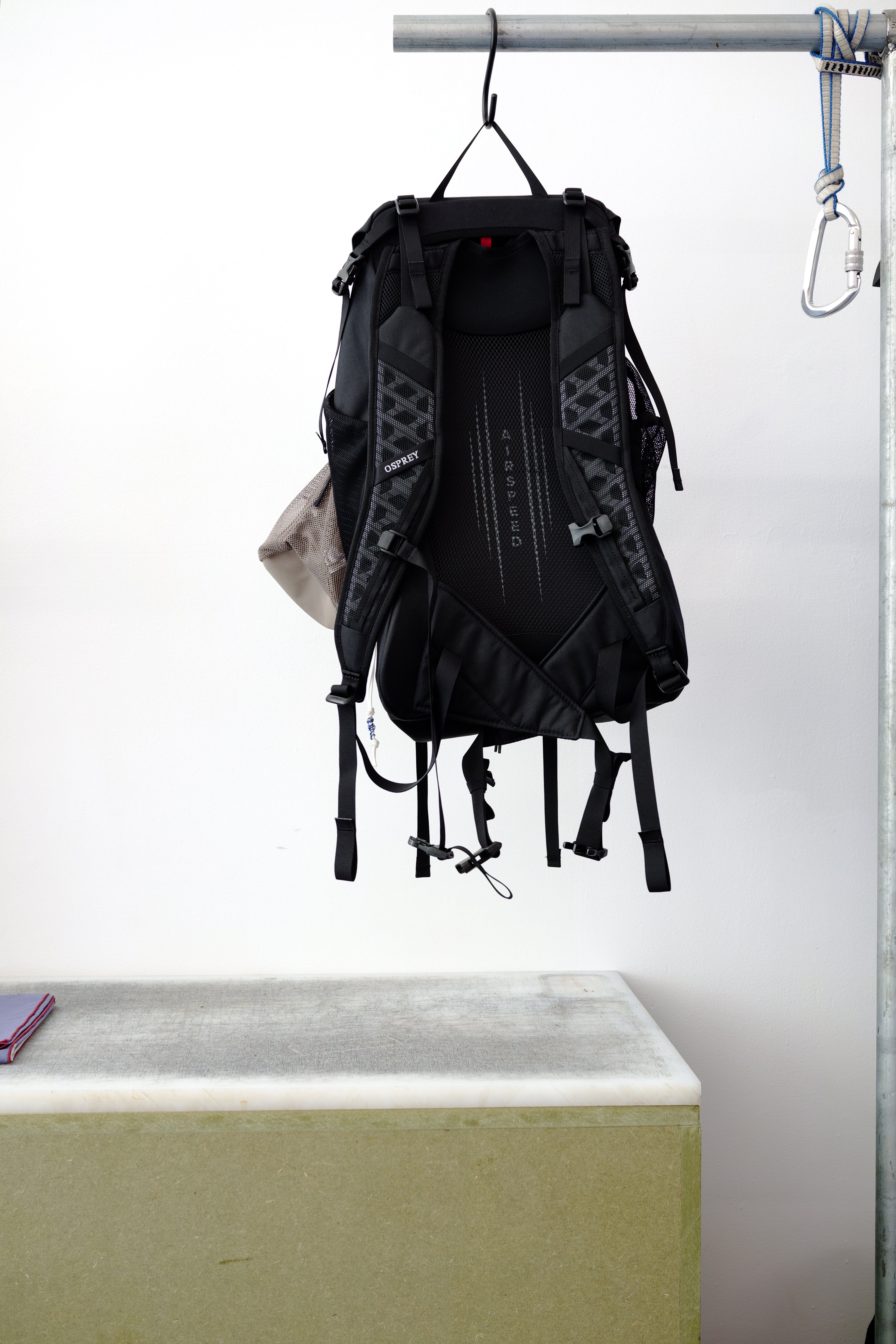 Black backpack hanging against a white wall, with small accessories tucked into the side pockets.