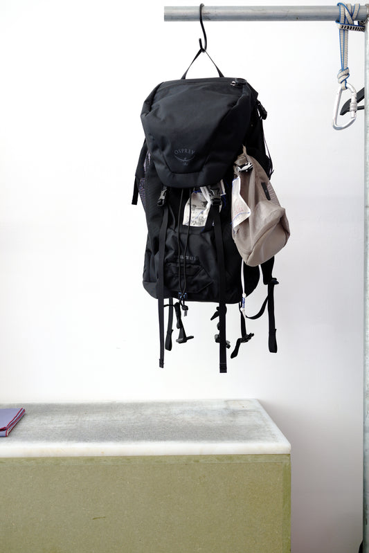 Black backpack hanging against a white wall, with small accessories tucked into the side pockets.