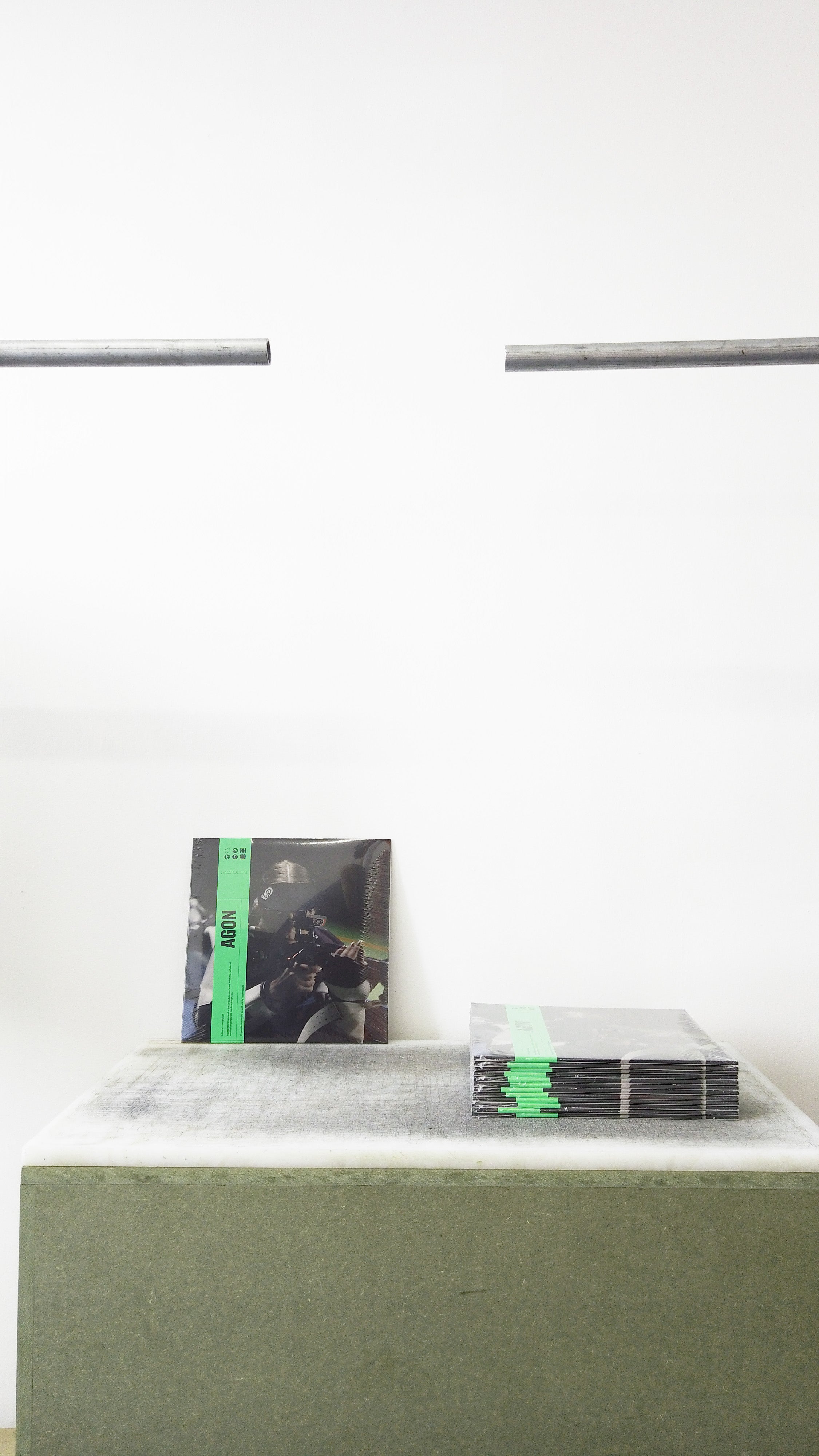 Small vinyl cases on a gray pedestal next to a stack of small vinyl cases, against a plain white wall.
